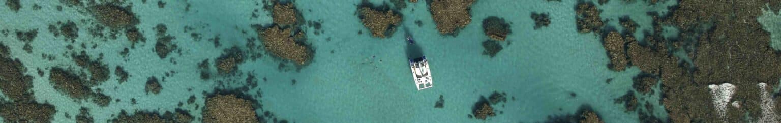 Aerial view of Shore Thing sailing catamaran surrounded by coral outcrops